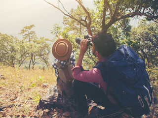 The tourist couple sitting use binoculars on the mountain.