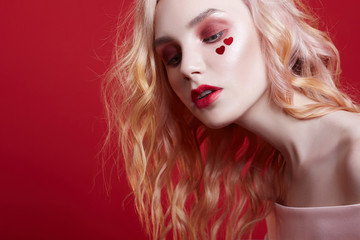 Fototapeta premium Portrait of sexy fashion beautiful blonde woman with bright makeup posing on red crimson background. Slender blonde girl, perfect figure and long hair. Clean perfect face skin