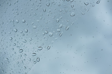Difference size of raindrops on glass window of car with cloudy sky in the background