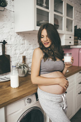 Pretty pregnant woman in kitchen with cup of milk