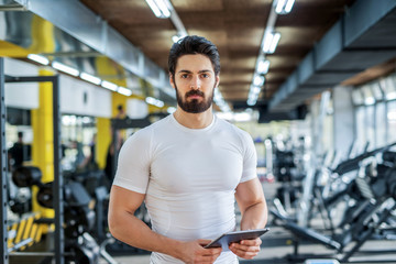 Fototapeta premium picture of strong handsome personal fitness trainer posing in front of the camera in bright gym.