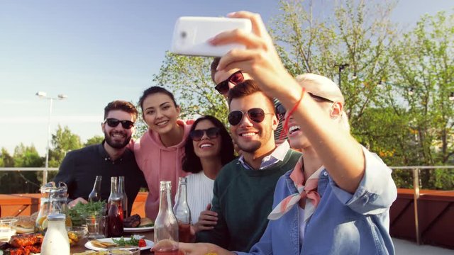 leisure and people concept - happy friends having bbq party on rooftop in summer and taking selfie by smartphone