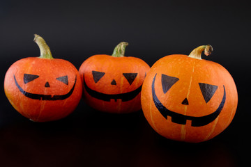 Pumpkins with painted faces on black background. Halloween backdrop.