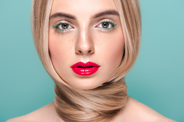 portrait of beautiful young woman with stylish makeup and long hair looking at camera isolated on blue