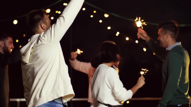leisure, celebration and people concept - happy friends with sparklers dancing at rooftop party at night