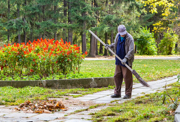 A middle-aged man in a gray and blue work jacket brown pants blue cap and gray gloves with a broom...
