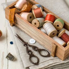 Fototapeta na wymiar Needlework. A small wooden box with old spools of sewing thread, a piece of cloth, scissors and a thimble on the table. 