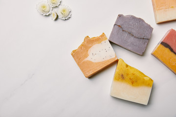 top view of various handmade soap pieces with flowers on white marble surface