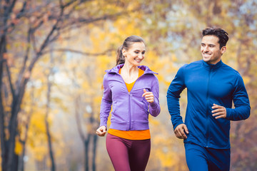 Man and woman running as fitness sport in an autumn park with colorful foliage