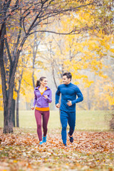 Man and woman running as fitness sport in an autumn park with colorful foliage