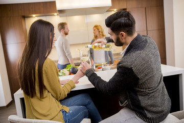 Group of young people having dinner and drinking wine in modern kitchen