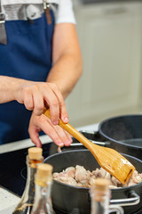 Man cooks meat in a frying pan. Hand using spatula to stir red and white frying pan full of meat