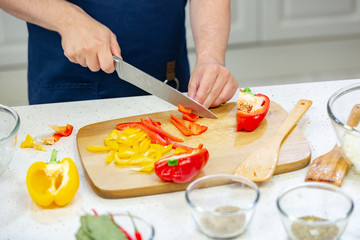 Men's hands cut red and yellow pepper on the wooden board close up