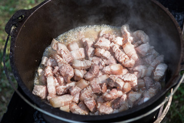 Meat is cooking in the pot on the fire for rice pilau. Camping in the nature and preparing food concept