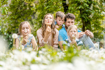 Family of five sitting on a meadow blowing dandelion flowers being happy and playful