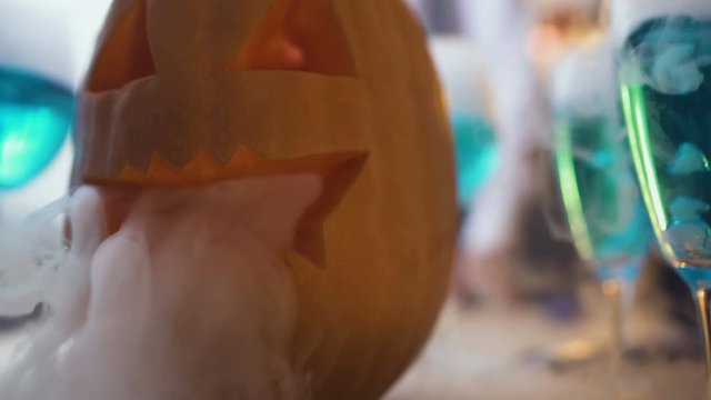 Carved jack lantern smoking, blue cocktails on Halloween party table, close-up