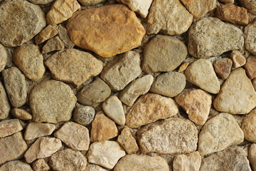 close up detail of stone work using smooth brown, sandy colored river stones of varying sizes on a rendered wall