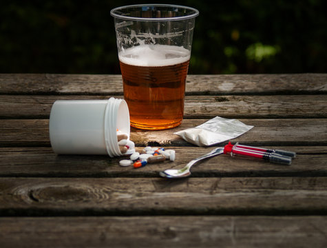 A glass of beer, pills, barbiturates, drugs, cocaine, heroin, a syringe and a spoon on a table. Drug addiction concept
