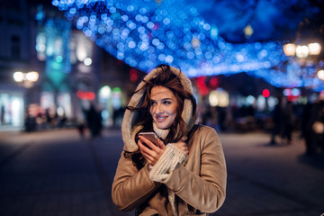 Beautiful smiling girl standing street in winter coat. Holding telephone and smiling. Christmas...