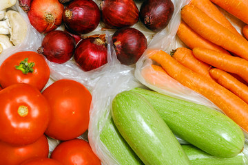Tomatoes, zucchini, carrots, red onions in plastic bags, focus on red onions. close-up.