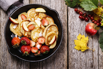 Cheese Buttermilk Pancakes or fritters with strawberry, sliced apples and coconut crunch on pan on vintage wooden table. Autumn breakfast