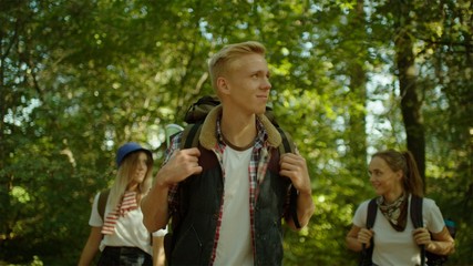 Group of hikers with backpacks and sticks walking in the forest