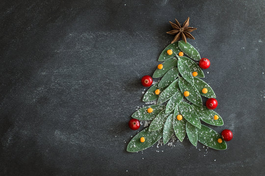 Fresh leaves of saffron lie on a dark background in the shape of a Christmas tree with cranberries