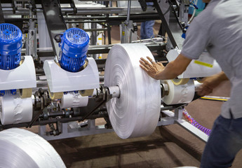 Industrial worker install roll of film material for plastic bag extruder machine. Process of...