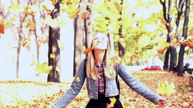 Happy, beautiful woman throwing golden leves in the autumn park, super slow motion
