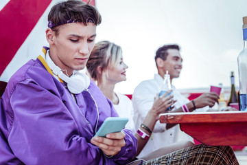 Low spirits. Negative delighted student crossing arms on chest while staring at his gadget