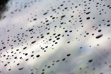Raindrops splatter on the glass of car window.