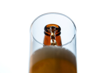 Perk view and close up. Beer poured from a bottle into a glass empty. On white background.
