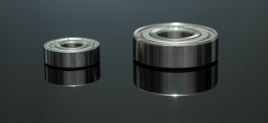 Close up view. Spare part is bearing placed on black glass floor. There is reflection with low light.