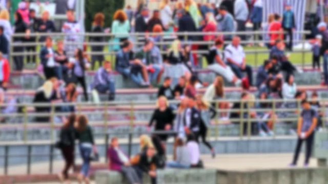 Blurred anonymous diverse crowd of people walking in groups on a festive fair on summer day.