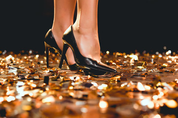 cropped view of woman in black high heels standing on golden confetti