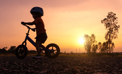 Obraz na płótnie Canvas Silhouette Asian kid first day play balance bike.