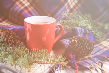Hot hot cup of coffee / tea on a wooden light background with a cozy winter blanket, branches of trees and cones, the concept of winter home comfort .Toned