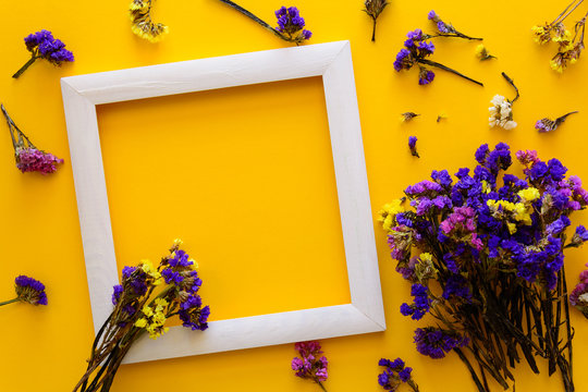 Colorful bouquet of dried autumn flowers lying on a white frame on yellow paper background. Copy space. Flat lay. Top view. Greeting card. Flowers composition.