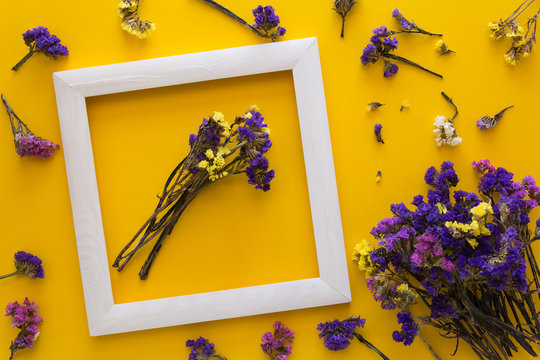 Colorful bouquet of dried autumn flowers lying on a white frame on yellow paper background. Copy space. Flat lay. Top view. Greeting card. Flowers composition.