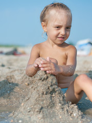 Fototapeta na wymiar Baby girl sitting on the sandy beach and playing near the sea. Summer vacations concept.