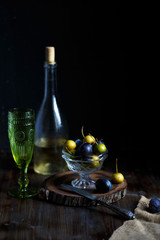 Obraz na płótnie Canvas Wild pear and plum in a glass bowl, a glass and a bottle of homemade pear wine on a wooden close background. Rustic concept.