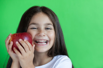 Happy child girl eat apple isolated on green background. Kid with fruits.
