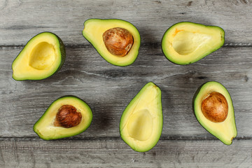 Tabletop view - arranged avocado halves, some of them with the seed, on gray wood desk.