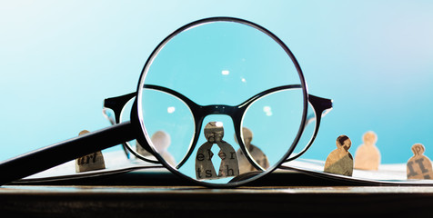 Business recruitment or hiring photo concept. Looking for talent. Icons of candidates are standing on open newspaper under magnifier.