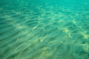 Ocean floor underwater photo, sand "dunes" lit by sunlight. Abstract marine background.