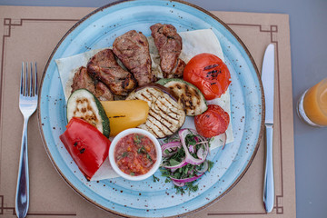 BBQ and grilled vegetables with salsa sauce on the beautiful blue plate in the restaurant. Minsk, Belarus.