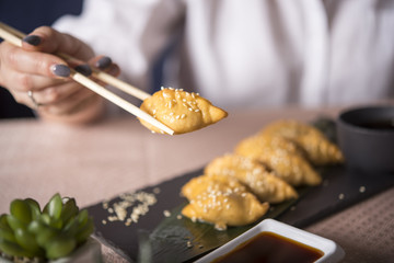 Close up fresh boiled dumplingss on stone slate. Chinese dumplings with sesame seeds on a green leaf. A woman eating dumplings using chopsticks. Photo with selective focus