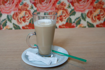 A large Cup of coffee with a saucer and a tube on the table. With sugar packets.