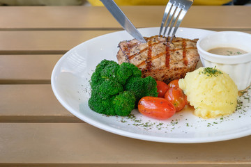Eating delicious grilled pork steak with Broccoli tomato and mash potato in White plate