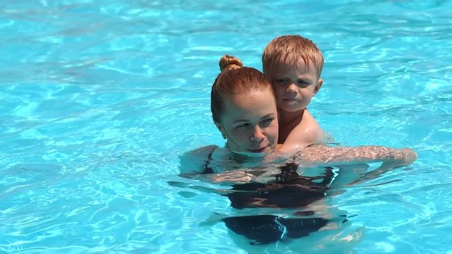 A cheerful family, a young mother with her son, have fun and play in the pool. They bathe, sunbathe and enjoy the hot weather in the hotel at the resort.